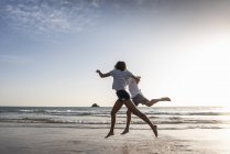Молода пара розважається на пляжі, бігає і стрибає в море — стокове фото