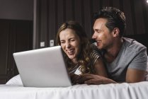 Щаслива пара лежав на ліжку вдома веселяться з ноутбуком — стокове фото