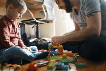 Father playing with building bricks on the floor while his sad little son watching him — Stock Photo
