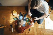 Father and son sitting on the floor playing together with building bricks, top view — Stock Photo