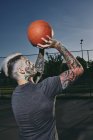 Hombre joven tatuado lanzando baloncesto en la cancha al aire libre - foto de stock