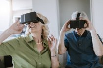 Senior couple at home sitting on couch wearing VR glasses — Stock Photo