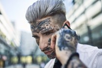 Joven hombre de negocios con cara tatuada, hablando por teléfono - foto de stock
