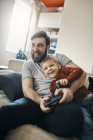 Ridendo padre e figlio piccolo seduti insieme sul divano a giocare al gioco per computer — Foto stock