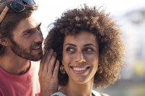 Счастливая молодая пара, мужчина шепчет женщине на ухо — стоковое фото