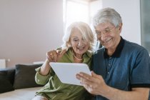 Felice coppia anziana a casa seduta sul divano tablet condivisione — Foto stock