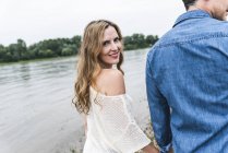 Улыбающаяся женщина идет рука об руку с мужчиной на берегу реки — стоковое фото
