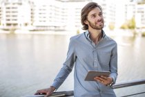 Jeune homme debout à garde-corps tenant tablette numérique — Photo de stock