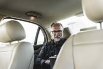 Uomo d'affari maturo seduto sul sedile posteriore in auto, utilizzando tablet digitale — Foto stock