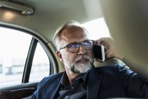 Uomo d'affari maturo seduto sul sedile posteriore in auto, parlando al telefono — Foto stock