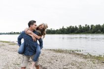 Homme portant copine piggyback au bord de la rivière — Photo de stock