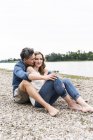 Couple affectueux assis au bord de la rivière — Photo de stock