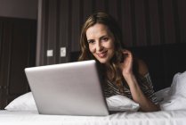 Smiling woman lying on bed at home looking at laptop — Stock Photo