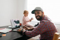 Vater arbeitet von zu Hause aus, benutzt Laptop, während sein Messgerät auf dem Schreibtisch sitzt und spielt — Stockfoto