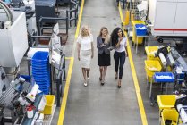 Três mulheres sorridentes com tablet andando no chão da fábrica — Fotografia de Stock