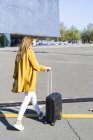 Вид ззаду жінка з валізою в місті, що йде по дорозі — стокове фото
