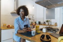 Mujer desayunando en su cocina, usando smartphone - foto de stock