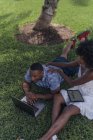 Giovane coppia che utilizza tablet e laptop sul prato in un parco — Foto stock