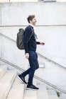 Улыбающийся взрослый мужчина с рюкзаком, спускающийся по лестнице по городу — стоковое фото