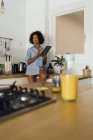 Woman sitting on worktop of her kitchen, using digital tablet in the morning — Stock Photo