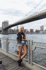 Estados Unidos, Nueva York, Brooklyn, mujer joven parada en el paseo marítimo y comiendo un helado - foto de stock