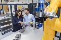 Colegas na empresa de alta tecnologia que controla robôs industriais, usando tablet digital — Fotografia de Stock