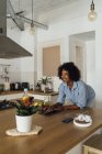 Mulher usando tablet digital e tomando um café da manhã saudável em sua cozinha — Fotografia de Stock