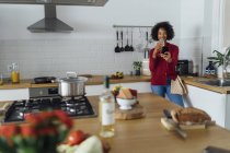 Donna in piedi nella sua cucina, facendo un selfie, bevendo vino — Foto stock