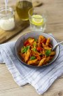 Penne with tomato and basil leaves in bowl with spoon on table — Stock Photo