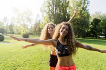 Portrait of happy twin sisters with arms outstretched in a park — Stock Photo