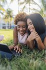 Retrato de duas amigas felizes relaxando em um parque e usando um tablet — Fotografia de Stock