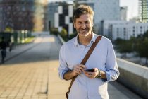 Retrato de hombre maduro sonriente con teléfono celular en la ciudad - foto de stock