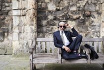 Портрет добре одягнений старший бізнесмен з сонцезахисні окуляри і навушники, сидячи на лавці — стокове фото