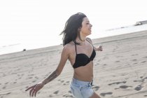 Giovane donna felice con tatuaggio e piercing al naso che corre sulla spiaggia — Foto stock