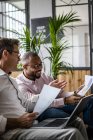 Two businessmen using laptop and discussing documents on sofa in loft office — Stock Photo