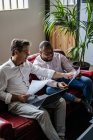 Two businessmen using laptop and discussing documents on sofa in loft office — Stock Photo