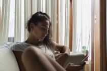 Молода жінка вдома сидячи на дивані і за допомогою смартфона — стокове фото