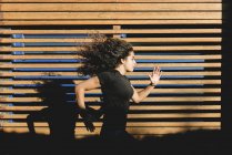 Sportive young woman running along wood paneling — Stock Photo