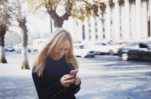 Smiling blond woman using smartphone in the city — Stock Photo