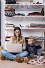 Llittle daughter watching mother sitting on the floor at home, using laptop — Stock Photo
