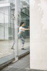 Young woman doing stretching exercise at glass facade — Stock Photo