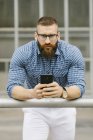 Portrait d'homme d'affaires barbu hipster avec smartphone appuyé sur une rampe — Photo de stock