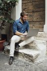 Lachender Geschäftsmann sitzt auf Stufen im Hof und benutzt Laptop — Stockfoto
