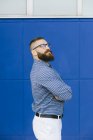 Retrato de hombre de negocios hipster barbudo con camisa a cuadros y de pie frente al fondo azul - foto de stock