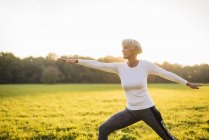 Seniorin macht Yoga auf der Wiese bei Sonnenuntergang — Stockfoto