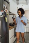 Женщина на кухне утром, используя смартфон — стоковое фото