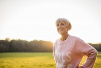 Smiling senior woman standing on rural meadow at sunset — Stock Photo
