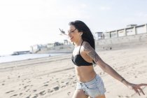 Mujer joven feliz con tatuaje corriendo en la playa - foto de stock