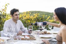 Italy, Tuscany, Siena, young couple having dinner in a vineyard with red wine — Stock Photo