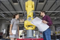 Бізнесмен і жінка, що мають зустріч перед промисловими роботами у високій технологічною компанією — стокове фото